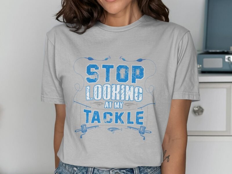A woman wears a gray t-shirt with blue text that reads, "STOP LOOKING AT MY TACKLE," with fishing graphics.