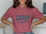 Woman wearing a red t-shirt with "CAMP Crew" printed in blue. She smiles and poses with hands on her hips.