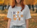 A woman in a gray t-shirt with "Happy Halloween" graphic, surrounded by autumn foliage.