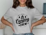 A woman wearing a grey t-shirt with a "Camping Crew" graphic and campfire design, displaying a friendly smile.