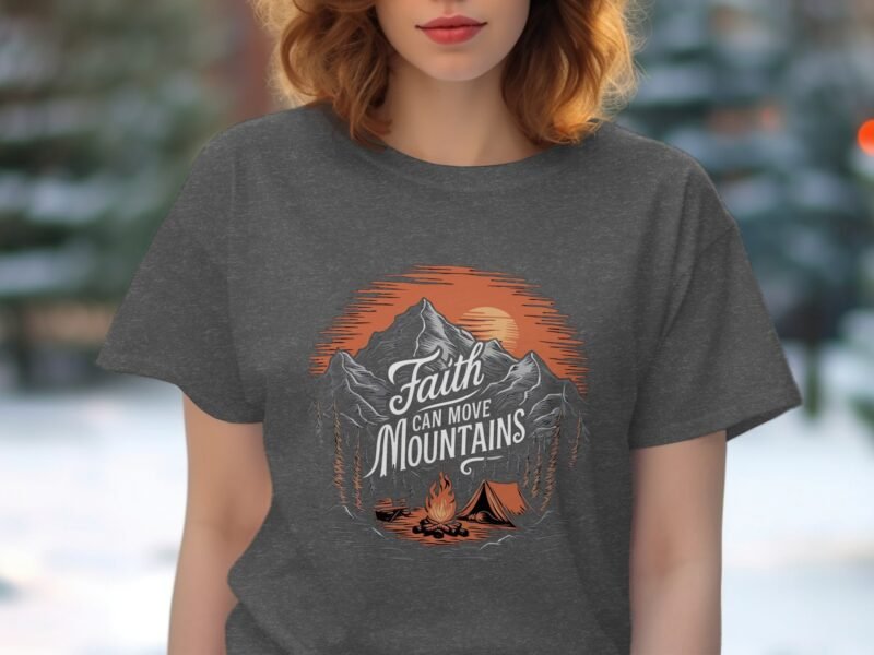 Woman wearing a gray t-shirt with a mountain graphic and the text "Faith can move Mountains." Background blurred.