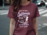 Maroon t-shirt featuring "California Surf's 1984" graphic, Malibu Beach, surfer silhouette, and beach-themed text.