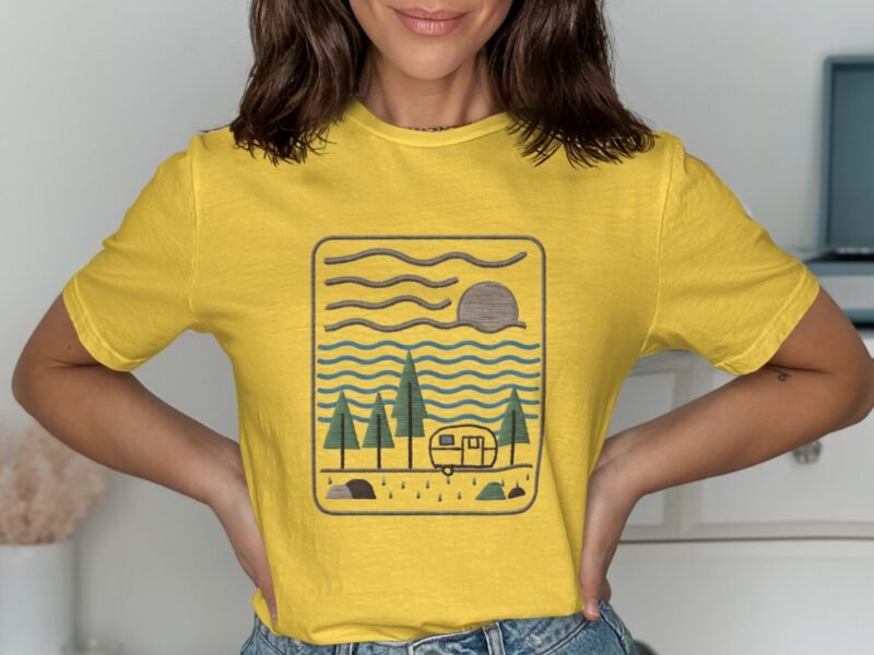 A woman in a yellow t-shirt with a camping scene illustration featuring trees, a trailer, sun, and waves.