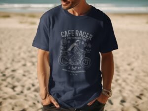 A man in a navy blue t-shirt with a motorcycle graphic stands on a beach, with ocean waves and sand in the background.