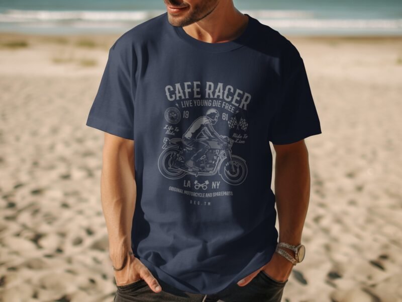 A man in a navy blue t-shirt with a motorcycle graphic stands on a beach, with ocean waves and sand in the background.