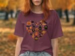 A woman with red hair wears a maroon t-shirt featuring a heart design filled with Halloween icons against an autumn backdrop.