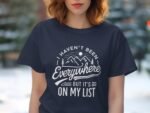 Navy t-shirt with text design: "I haven't been everywhere, but it's on my list" featuring mountains and sun graphics.