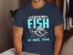 A person wearing a navy t-shirt with the text "I CATCH MY FISH IN REEL TIME" and a fishing graphic.