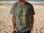 Man wearing a green t-shirt with football graphics and text about championships, standing on a sandy beach.