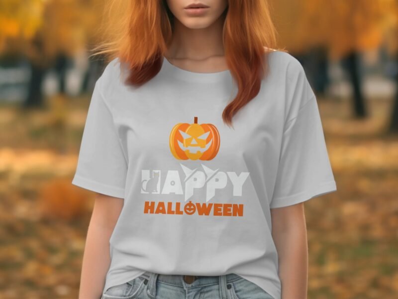 Woman in a light gray t-shirt with "Happy Halloween" and a pumpkin design, set against a fall landscape.