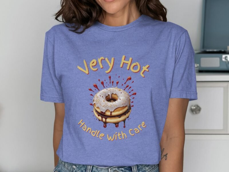 A person wearing a light blue t-shirt with a donut graphic and text reading "Very Hot Handle With Care."