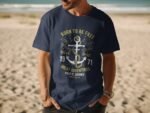 Man wearing a navy blue t-shirt with an anchor design and the text "Born to be Free" on a sandy beach.