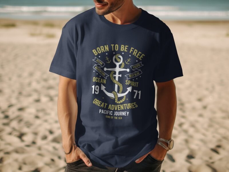 Man wearing a navy blue t-shirt with an anchor design and the text "Born to be Free" on a sandy beach.