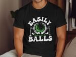 A man wearing a black t-shirt with the phrase "Easily Distracted By Balls" and a golf-themed graphic.