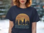 A woman wears a navy t-shirt featuring a graphic of pine trees against a stylized sunset.