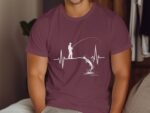 A person in a maroon shirt with a white fishing design and heartbeat line, sitting on a couch.