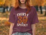 A woman with reddish hair wears a maroon t-shirt that reads "THIRTY 30 & SPOOKY," set against an autumnal background.
