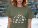 A woman in a green t-shirt with "Hike More Worry Less" and mountain graphic, standing outdoors.