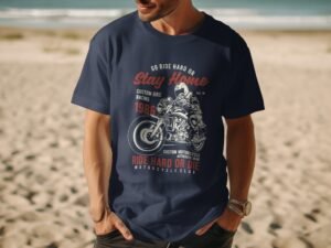 A man wears a navy blue t-shirt featuring motorcycle graphics and text about riding, set against a beach backdrop.