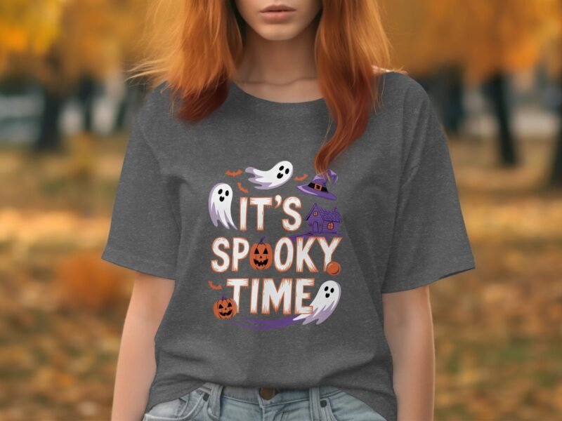 A person with reddish hair wearing a gray t-shirt that says "It's Spooky Time," surrounded by autumn foliage.