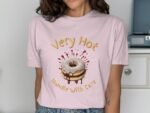 A woman wearing a pink t-shirt with an illustration of a donut and the words "Very Hot Handle With Care."