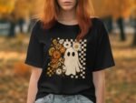 Woman with red hair wearing a black t-shirt featuring a ghost and floral design, set in an autumn landscape.