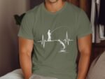 A man wearing an olive green shirt with a white graphic design of a fisherman and a leaping fish over a heartbeat line.