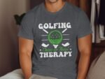 Man wearing a gray t-shirt with "Golfing Cheaper Than Therapy" printed, featuring a green golf ball graphic.