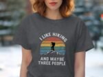 Woman wearing a dark gray t-shirt with a hiking-themed graphic and text: "I LIKE HIKING AND MAYBE THREE PEOPLE."
