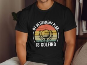 Black t-shirt with the text "MY RETIREMENT PLAN IS GOLFING" and a graphic of a golf ball on a colorful sunset background.