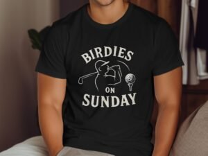 A man wearing a black t-shirt with the text "BIRDIES ON SUNDAY" and a golfer graphic, sitting indoors.