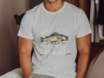 A man in a white t-shirt featuring a cartoon fish and the text "Mine's so big I have to use two hands."