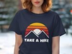 A woman in a navy t-shirt with a sunset and mountain graphic, featuring the text "TAKE A HIKE."