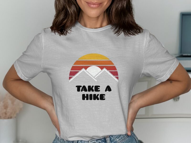 Woman wearing a gray t-shirt featuring a sunset and mountains graphic with the text "TAKE A HIKE."