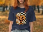 Model wearing a navy t-shirt featuring a Halloween-themed graphic with a pumpkin and daisies on a checkered background.