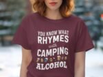 A woman in a maroon t-shirt with a humorous slogan about camping and alcohol, set against a blurred outdoor background.