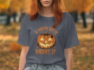 A woman in a gray t-shirt with a pumpkin graphic and the text "IF YOU'VE GOT IT, HAUNT IT" in a fall setting.