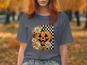 A woman in a gray t-shirt featuring a pumpkin design with flowers on a checkered background, autumn trees behind her.
