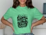 A person wearing a green t-shirt with a black graphic text design about life and mountains, smiling.