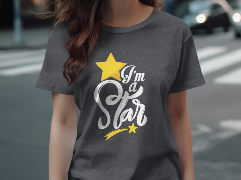 A woman wears a gray T-shirt featuring the phrase "I’m a Star" with a yellow star graphic, outdoors on a street.