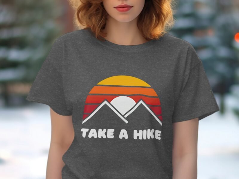 A woman in a gray t-shirt with a sunset and mountains design and the text "TAKE A HIKE" on it.