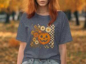 Person wearing a gray t-shirt with a pumpkin and floral graphic, set against a fall background of orange leaves.