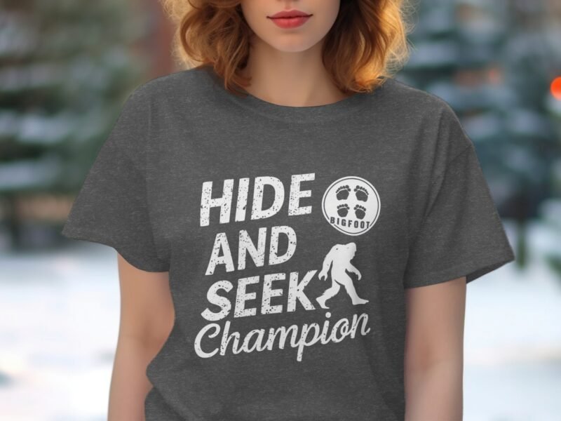 Woman wearing a gray t-shirt with the text "Hide and Seek Champion" and a Bigfoot illustration.