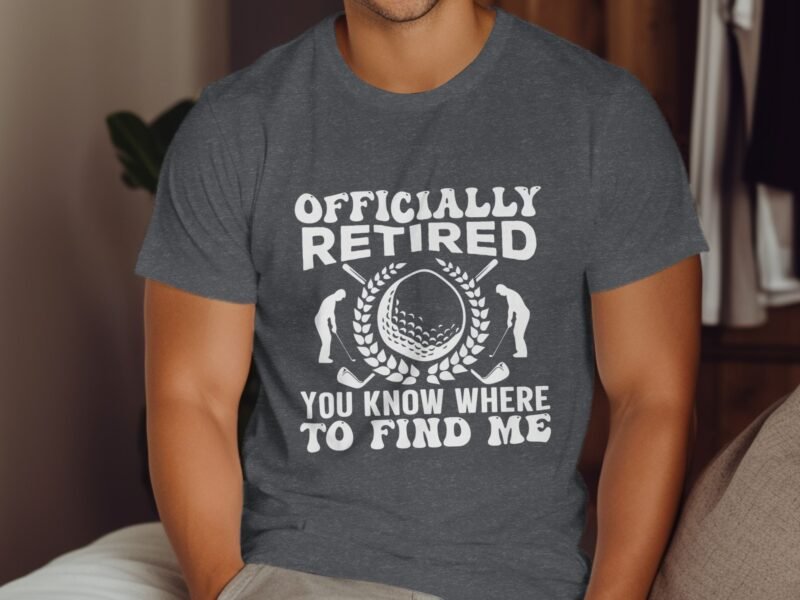 A man wearing a gray shirt with the text "Officially Retired" and golf-themed graphics, sitting indoors.