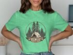 A woman is wearing a green t-shirt with a camp-themed design featuring a tent and trees.
