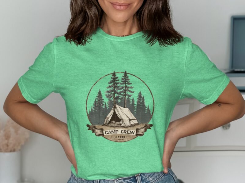 A woman is wearing a green t-shirt with a camp-themed design featuring a tent and trees.