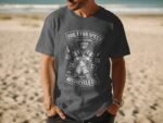 Man wearing a gray t-shirt with a motorcycle-themed graphic, set against a sandy beach background.