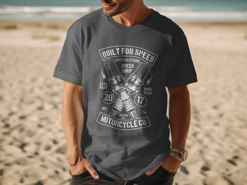 Man wearing a gray t-shirt with a motorcycle-themed graphic, set against a sandy beach background.